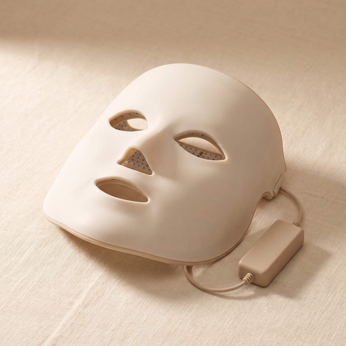 Le Masque La Pénombre, silicone souple, posé à plat sur du lin, éteint, avec son boîtier de commande